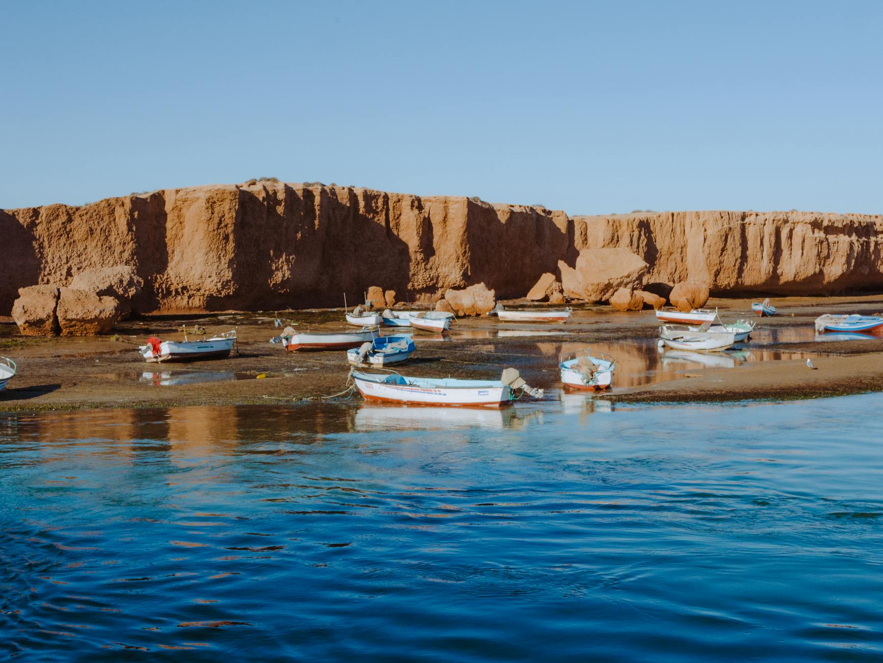 Najpiękniejsze zatoki i plaże Tunezji dostępne tylko łodzią: gdzie ich szukać i jak tam legalnie dopłynąć Łodzie rybackie na spokojnej wodzie u skalistego wybrzeża Tunezji